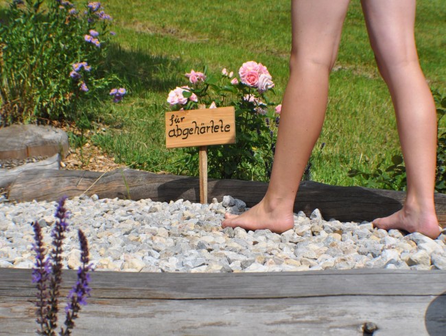 Barfußgehende Person auf einem Kiesweg mit Schild "für Abgehärtete" im Garten