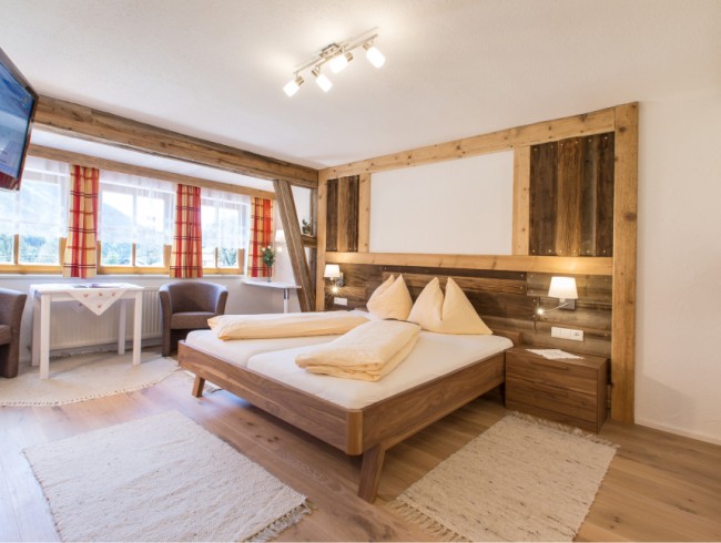 Gemütliches Hotelzimmer mit Doppelbett, Holzwänden und Fenstern mit Bergblick