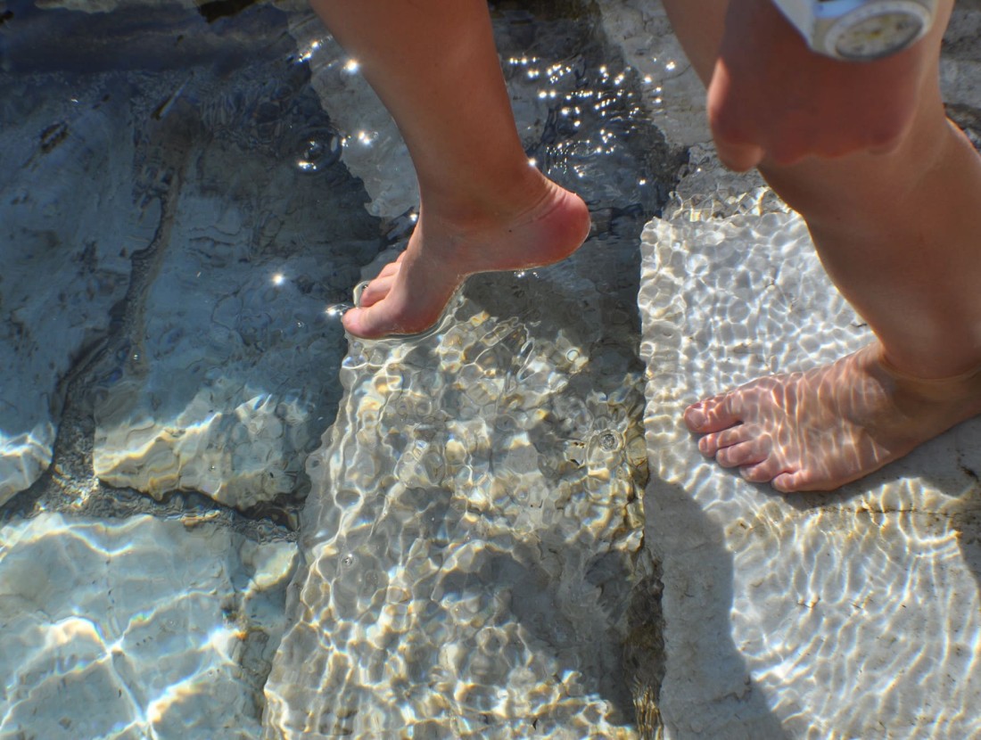 Eine Person geht barfuß durch flaches, klares Wasser auf Steinen