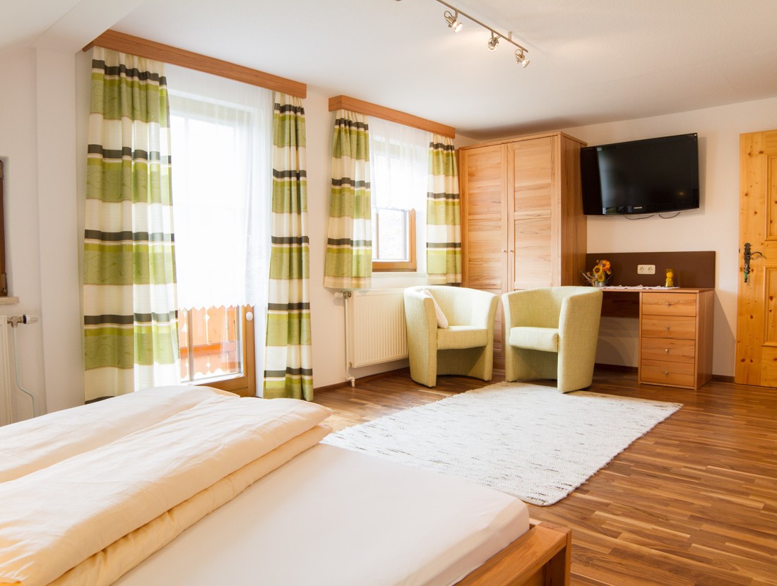 Helles Schlafzimmer mit Holzmöbeln, zwei grünen Sesseln und Streifenvorhängen